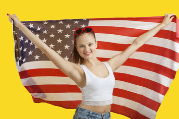 Fototapeta premium Portrait of happy young woman holding American flag over yellow background
