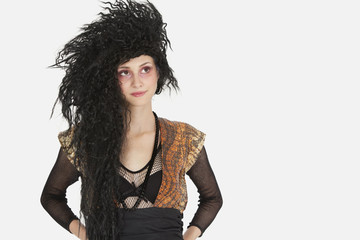 Beautiful young Goth woman with teased hair looking away over gray background