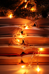 Pile of open books, coniferous branch and garland, closeup
