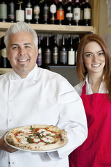 Portrait of a happy chef holding pizza with beautiful waitress