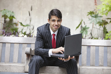 Young Indian businessman using laptop while sitting on bench