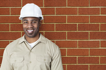 Portrait of happy young construction worker with hardhat over brick wall