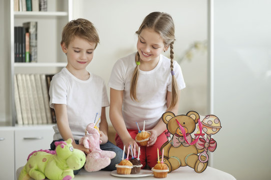 Siblings and soft toys celebrating birthday with cup cakes