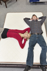 Friends lying on mattress with hands behind head in furniture store
