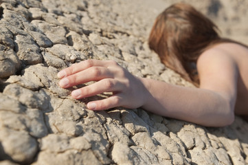 Woman lying on cracked land with focus on hand