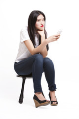 Naklejka premium Portrait of beautiful young woman in casuals sitting on stool with mobile phone against white background