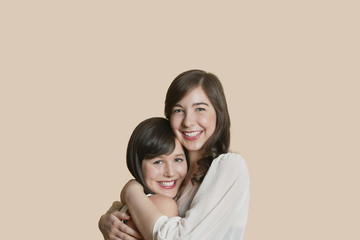 Portrait of young female friends hugging over colored background