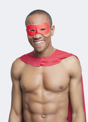 Portrait of young shirtless man in superhero costume smiling against gray background