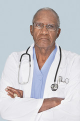 Portrait of a senior doctor with arms crossed over light blue background