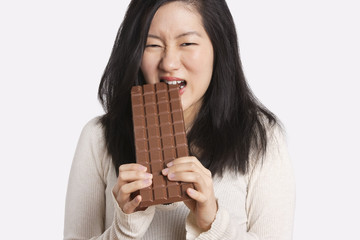 Portrait of a young woman eating a large chocolate bar over light gray background