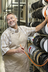 Fototapeta premium Happy mature salesperson standing by electrical wire spool while looking away in hardware store