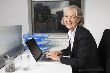 Portrait of smiling senior businesswoman using laptop at desk in office