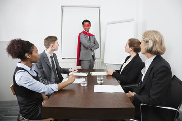 Business leader as superhero in front of colleagues at meeting in conference room