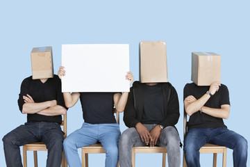 Man holding blank cardboard with male friends faces covered with boxes over blue background