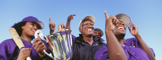 Obraz premium Panoramic shot of cheerful baseball players with trophy celebrating victory against clear sky