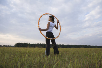 Rear view of fit woman holding hula hoop on field