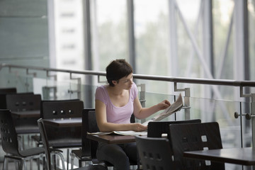 Young woman reading newspaper at cafe of shopping centre
