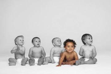 Baby girl sitting on floor with other babies looking away