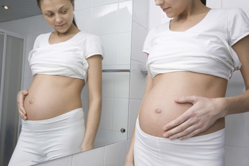Midsection of pregnant young woman standing in front of bathroom mirror