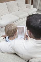 Rear view of relaxed father and son using digital tablet on sofa