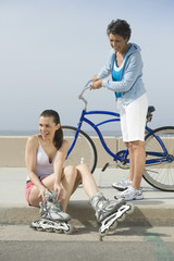 Full length of senior woman with bicycle looking at daughter putting on inline skates