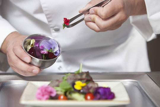 Midsection closeup of male chef arranging edible flowers on salad in commercial kitchen