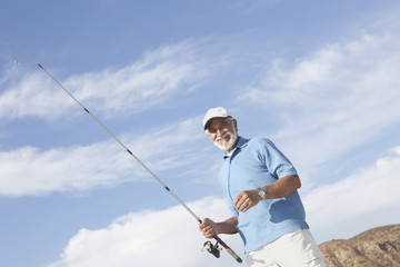 Portrait of a happy senior Caucasian man holding fishing rod against cloudy sky