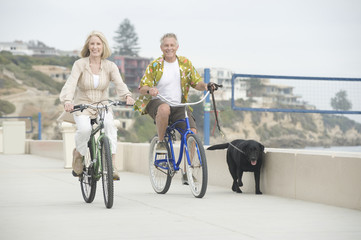 Happy senior couple riding bicycles with a dog