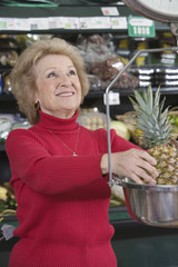 Smiling senior woman weighing pineapple in supermarket