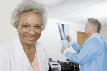 Portrait of a happy female doctor with colleague examining x-ray report in the background