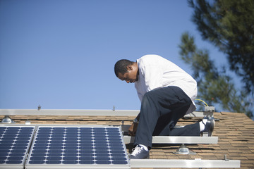 Full length side view of an African American man fixing solar panel on rooftop