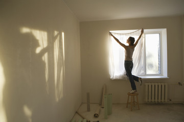 Full length rear view of young woman fitting curtain in new apartment