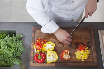 Midsection of male chef dicing red and yellow bell peppers in commercial kitchen