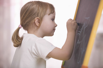 Side view of cute little girl drawing on chalkboard at home