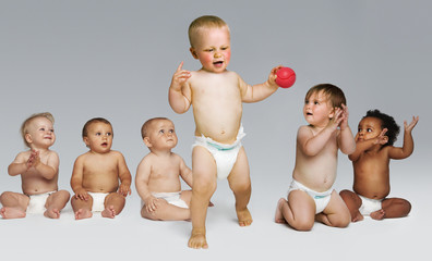Full length of babies looking at a toddler take first steps against gray background