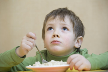 Unhappy cute boy eating food while looking up at table © MDBPIXS