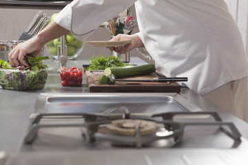 Midsection side view of male chef preparing salad in commercial kitchen