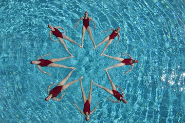 Group of synchronised swimmers forming a star shape in pool
