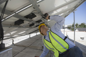 Young maintenance worker adjusting solar panels on rooftop