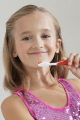 Portrait of young girl holding toothbrush against gray background