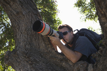 Closeup of a paparazzi photographer hiding behind tree