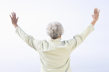 Rear view of a senior woman stands facing sea with arms raised