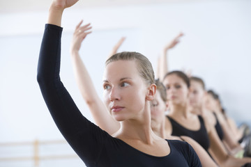 Beautiful young woman with classmates practicing at the barre in ballet rehearsal room © MDBPIXS
