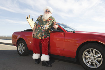 Father Christmas stands by red convertible with surfboard