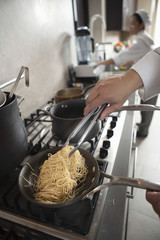Closeup of female chef preparing spaghetti with colleague working in background