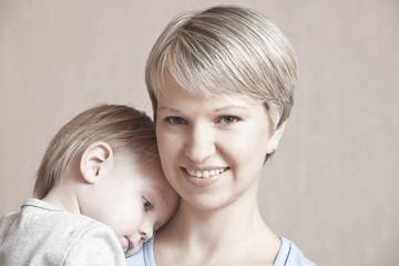 Portrait of smiling young mother with baby boy leaning on her shoulders over colored background