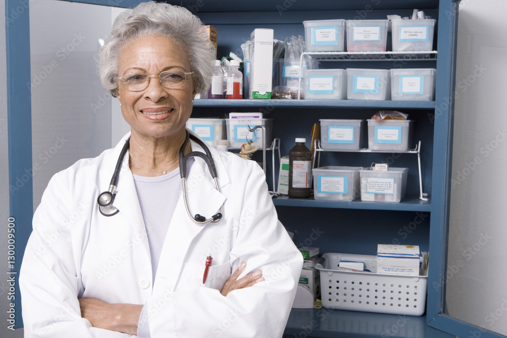 Wall mural Portrait of confident senior female doctor standing with hands folded in clinic