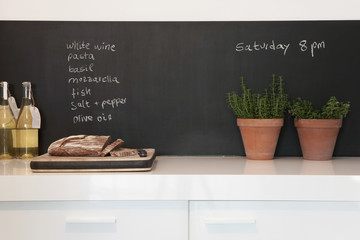 Bread on chopping board with shopping list written on blackboard in kitchen