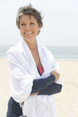 Happy senior woman wrapped in stole standing hands folded at beach