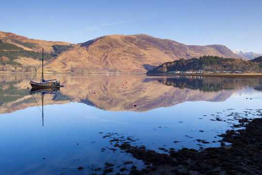 Picturesque tranquil Loch Leven with sailing boat and reflection from Glen Coe village, Highlands, Scotland